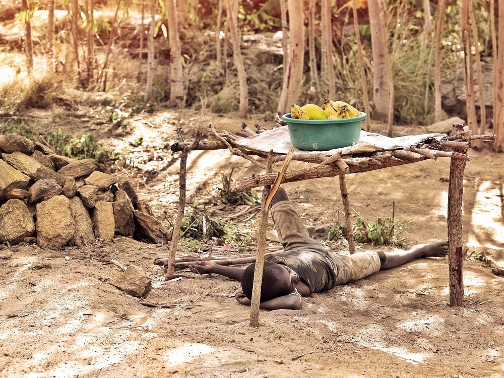 A young Kenyan boy takes shelter under the shed as he sells fruits on a hot day.