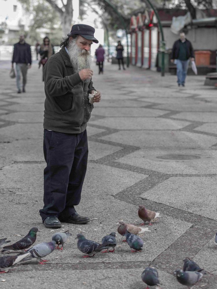 The beggar shares food with the pigeons