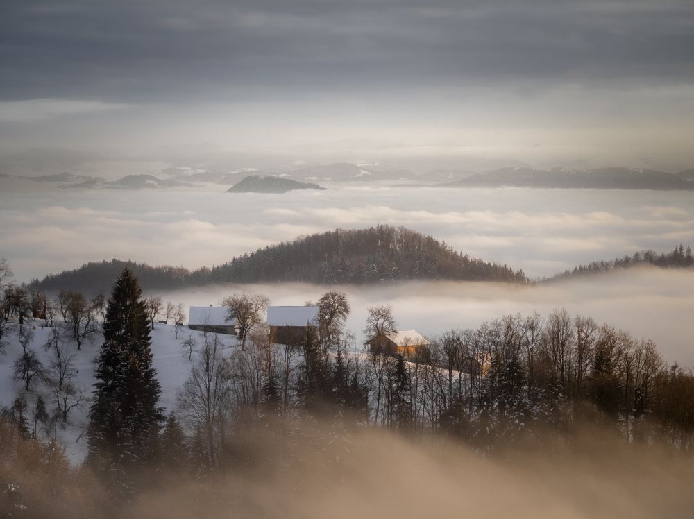 Sunset over small hill emerging from fog