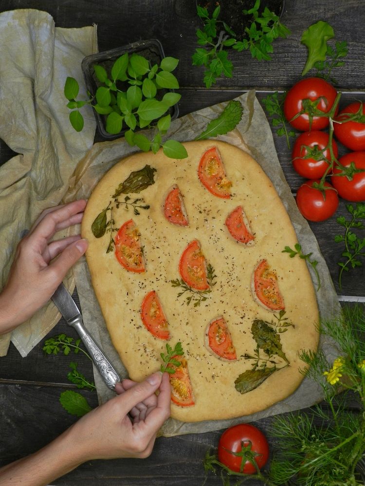 Focaccia with tomatoes and herbs. Hands in the frame!
