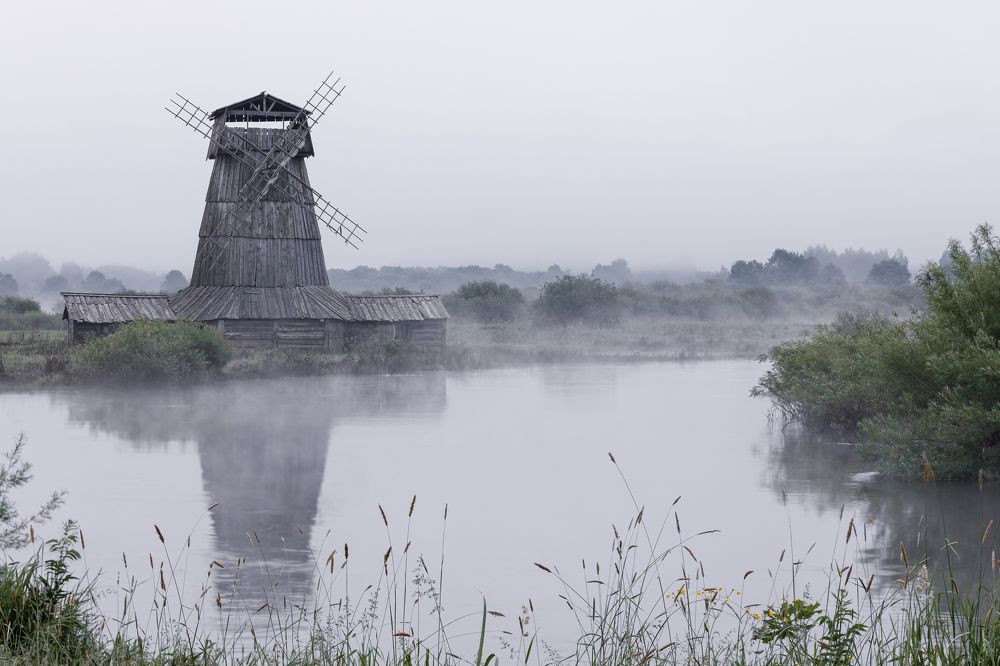 An old mill on the river in the fog in the early morning.