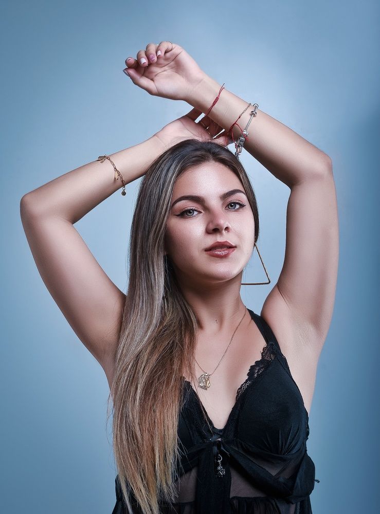 Portrait of young woman with raised hands on blue background