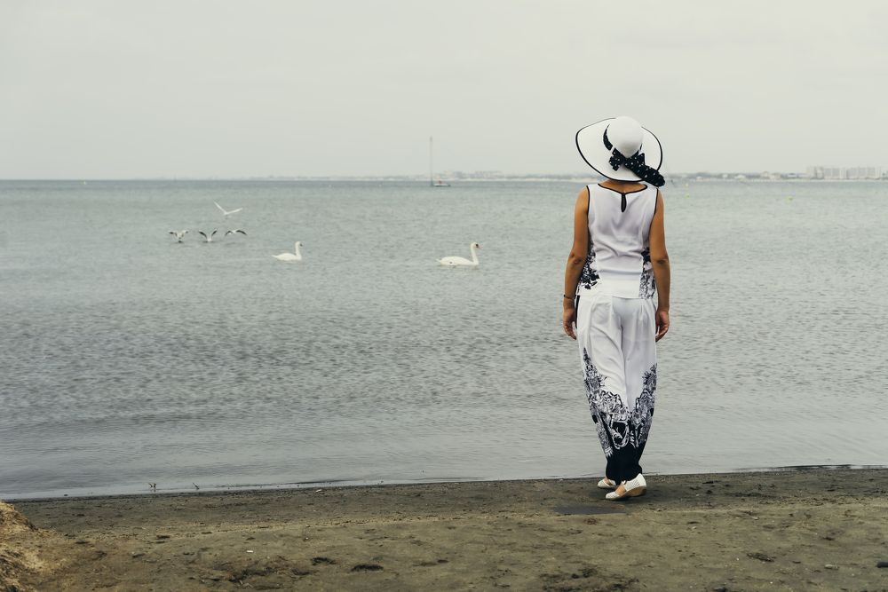 Девушка в белой шляпе смотрит в даль моря.
