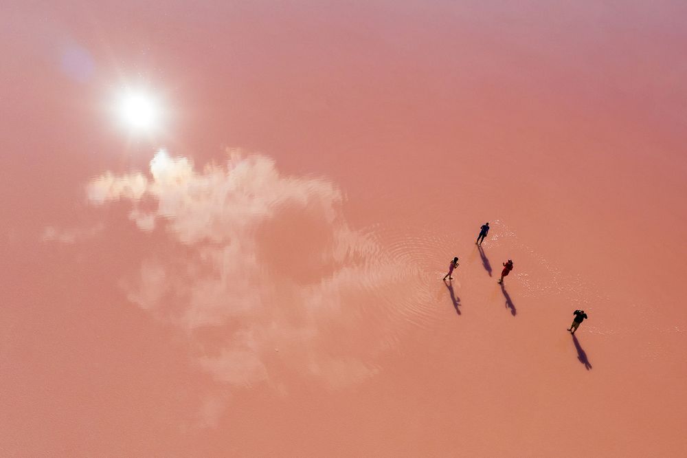 A few people stand on the pink surface of a salt lake.
