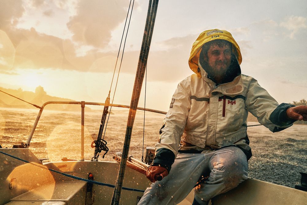 Репортажный снимок с прогулки на парусной яхте под ливнем с красивым закатный солнцем.