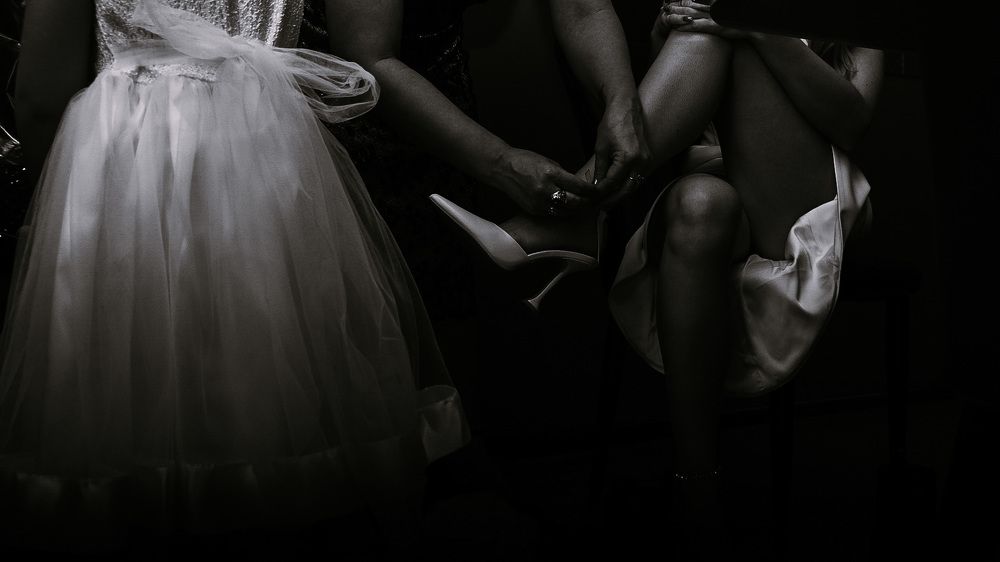 Мама невесты застегивает туфли дочери на свадьбе