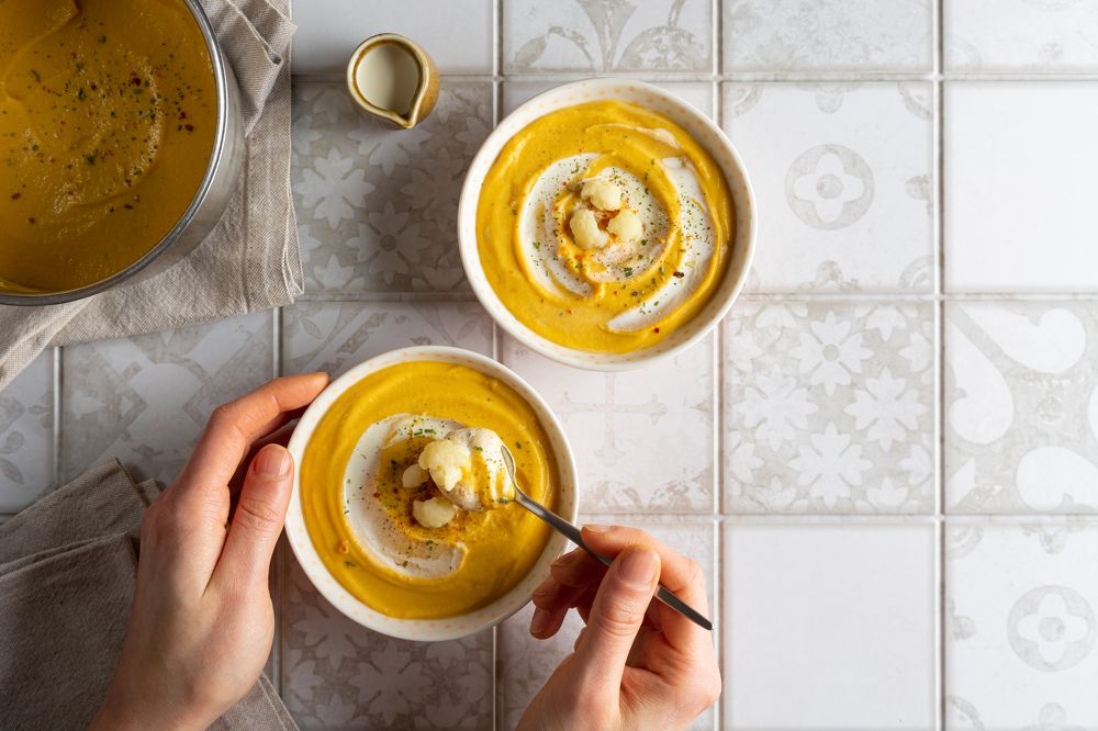 Woman eating carrot cream soup garnished with cauliflower and herbs