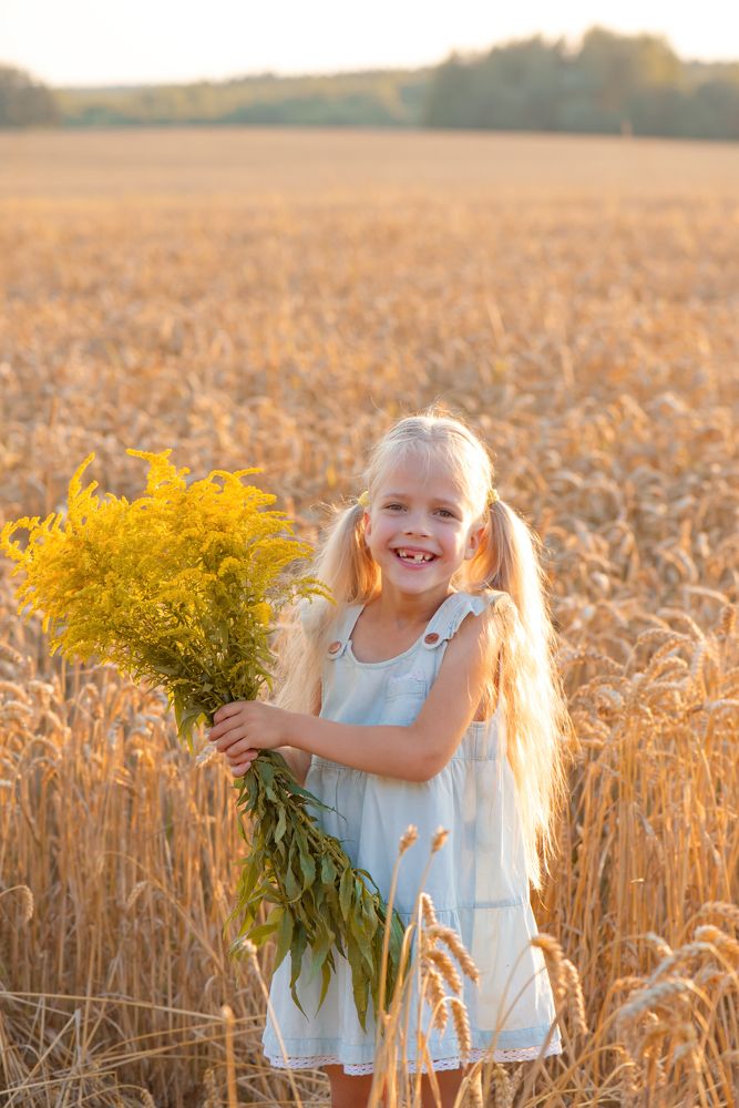 Улыбающаяся девочка с цветами на поле.