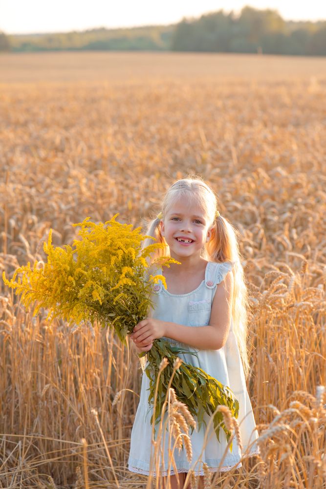 Улыбающаяся девочка с цветами на поле.