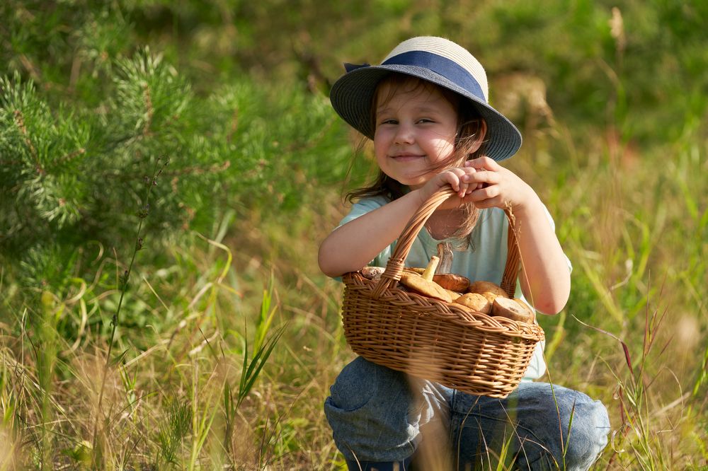 A girl in a straw hat with a basket of mushrooms.