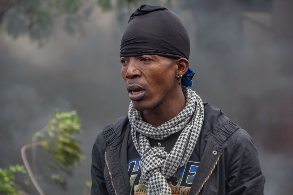 A photo taken while a man poses behind burning tires.