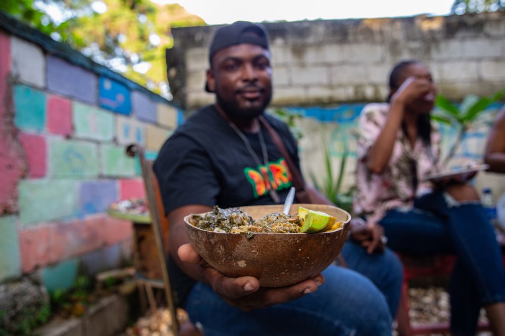 A man sitting on a chair holding in his hand a calabash full of food inside.
