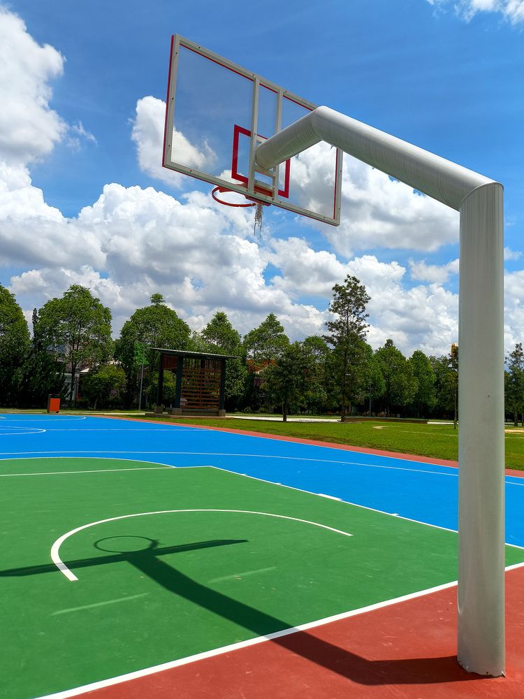 A basketball hoop on a blue court with trees in the background