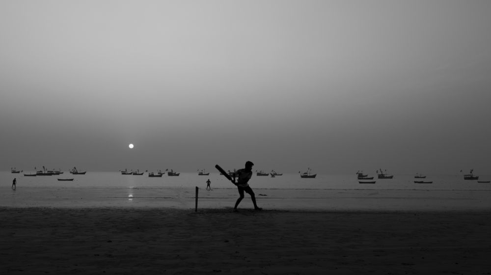 Boys playing cricket near seashore.