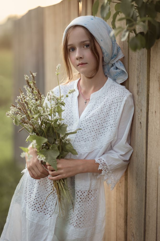 Девочка у забора с букетом полевых цветов.