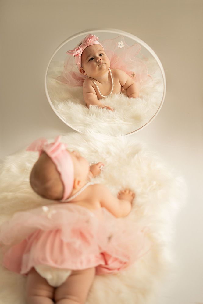 A child is lying on a white fluffy mat, there is a round mirror against it, in the mirror you can see the reflection of the child.