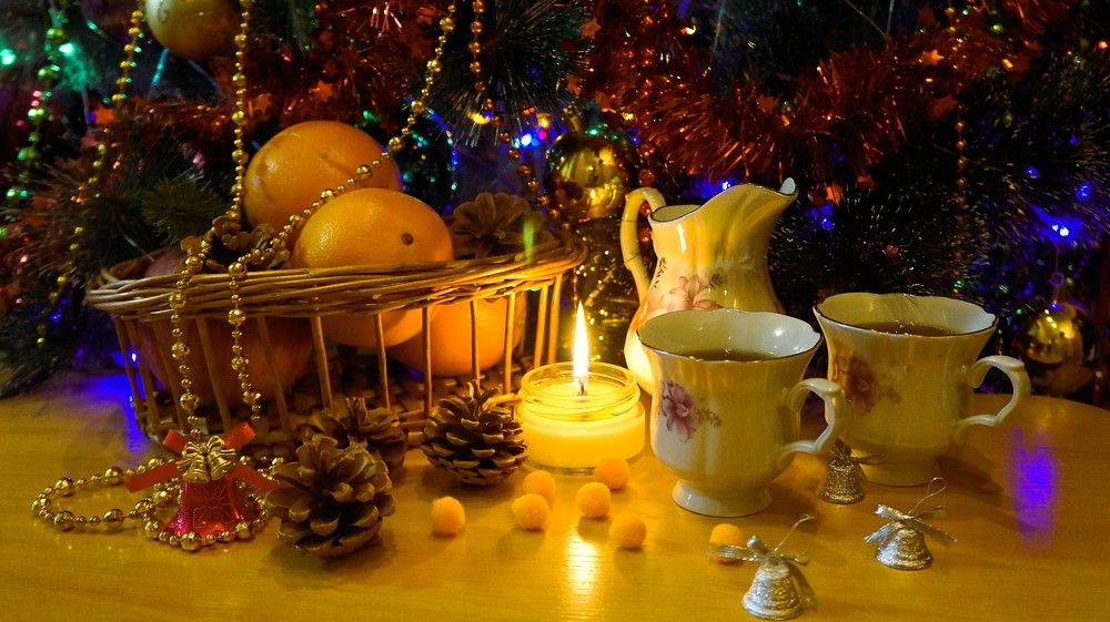 Зимний натюрморт с апельсинами, свечой, чаем и шишками под новогодней ёлкой