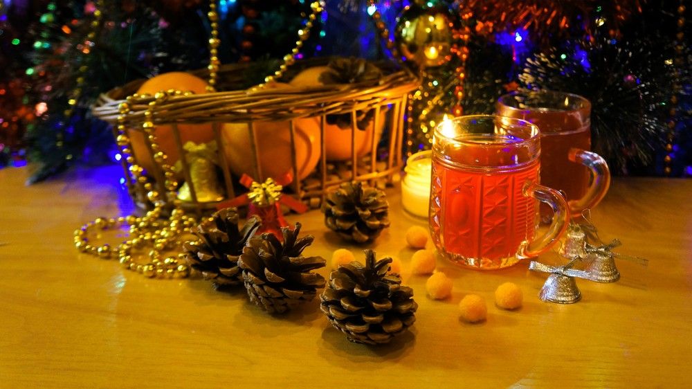 Зимний натюрморт с апельсинами, свечой, морсом и шишками под новогодней ёлкой