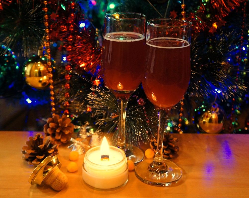 Зимний натюрморт со свечой, натуральным игристым (pétillant naturel) в хрустальном бокале и шишками под новогодней ёлкой