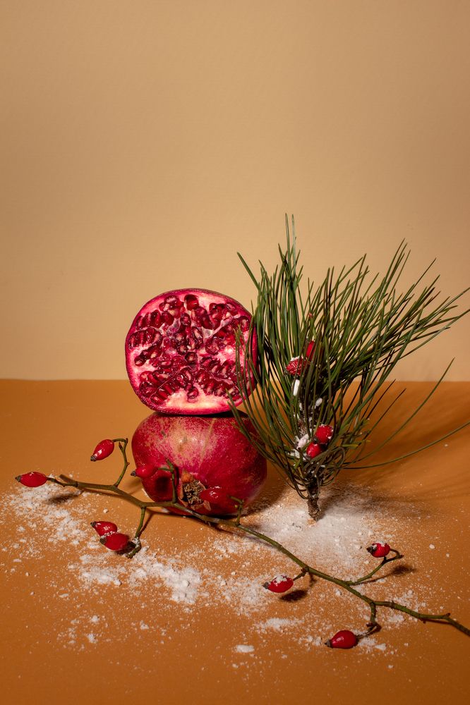 Pomegranate and evergreen branches against brown background.