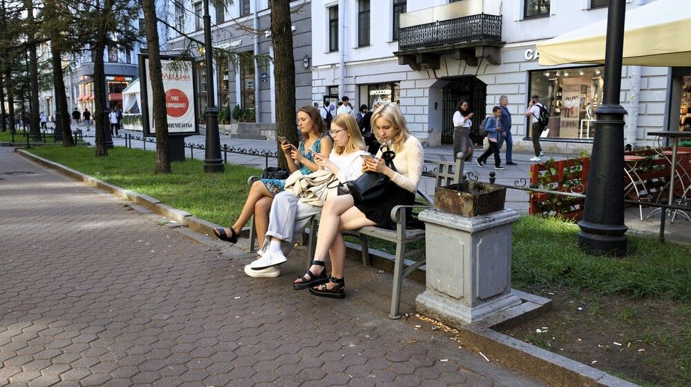 Three beautiful girls are watching something on their smartphone while relaxing on a bench
