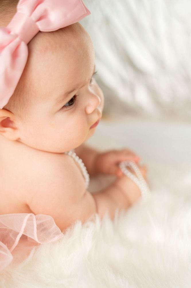 Portrait of an adorable baby girl with a pink headband and pearl necklace on a fluffy rug background