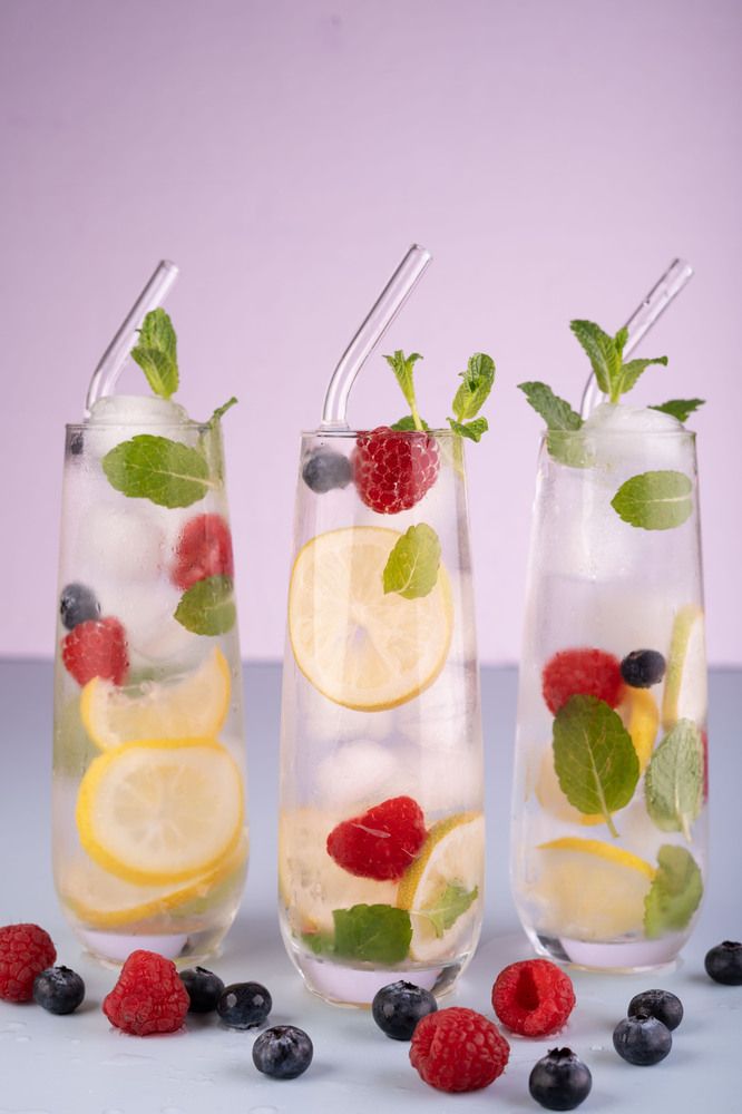 glasses of water with lemon, raspberry, and blueberry slices on a light background