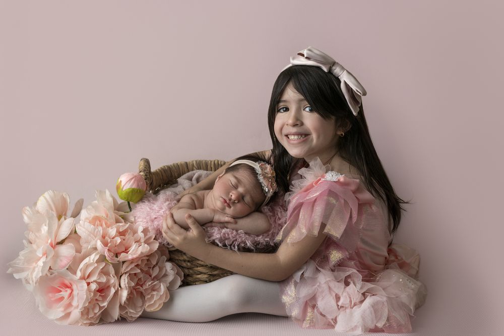 Newborn baby girl and her sister surrounded with pink flowers