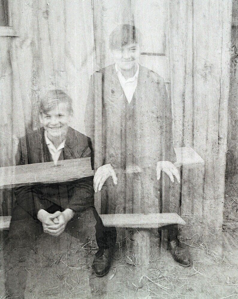 Двое молодых людей, сидящих на скамейке перед деревянным забором