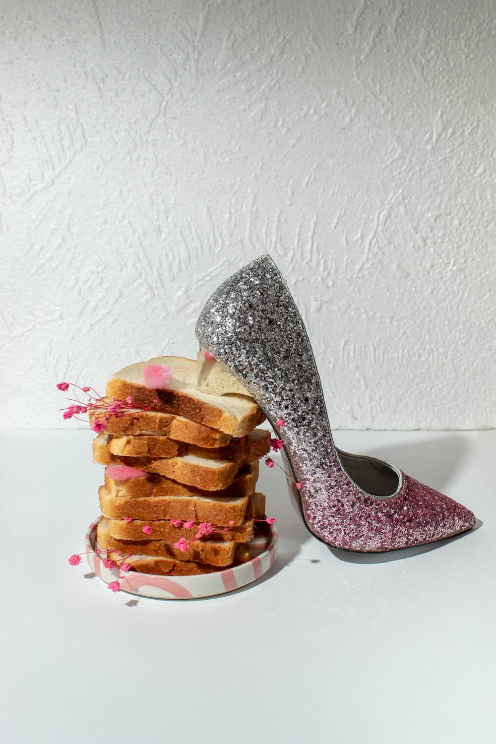 Pink glitter high heel shoe with stacked bread slices, surreal fashion still life concept