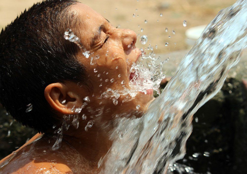 A boy drinks water from an irrigation tube, on a hot summer afternoon on the outskirts of Jammu