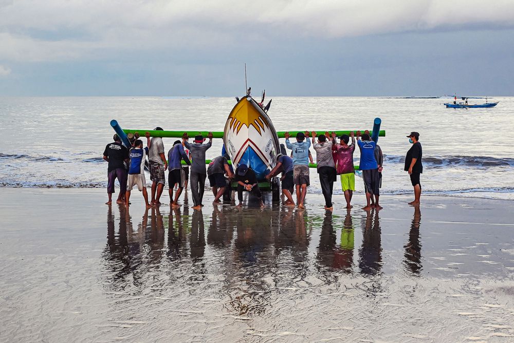 A group of fisherman dragging the boat to the shoreline.