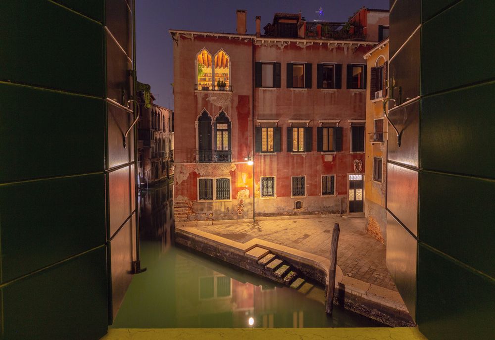 View of a Venetian canal through a window at night.