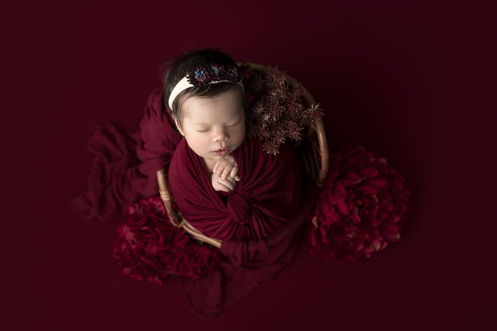 Newborn girl surrounded by red flowers