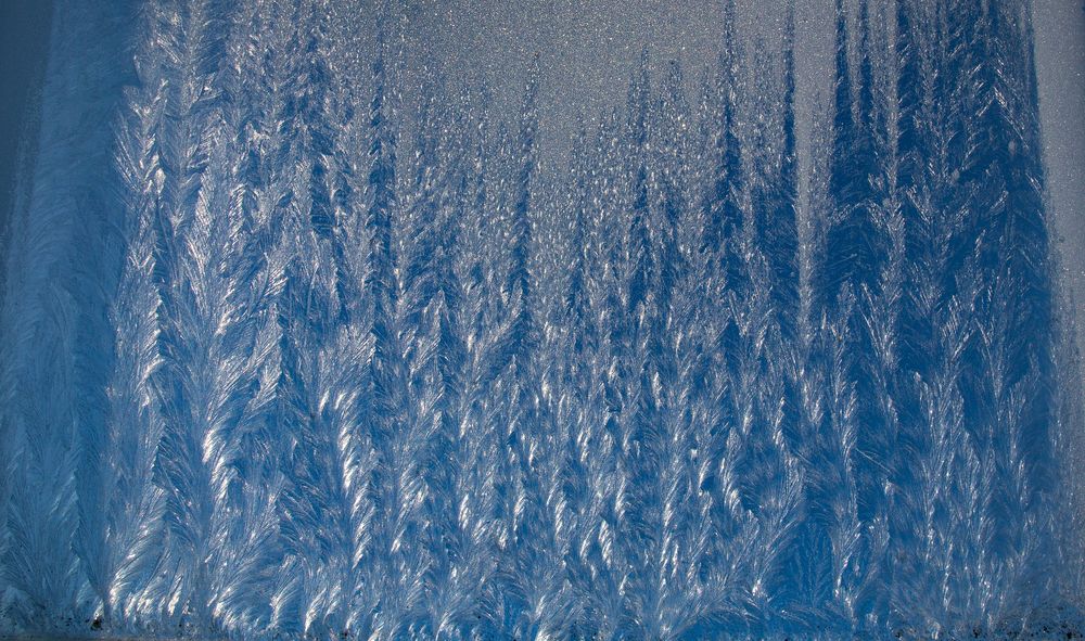 A beautiful frozen window glass covered with amazing natural ice patterns and frost textures on a cold winter day