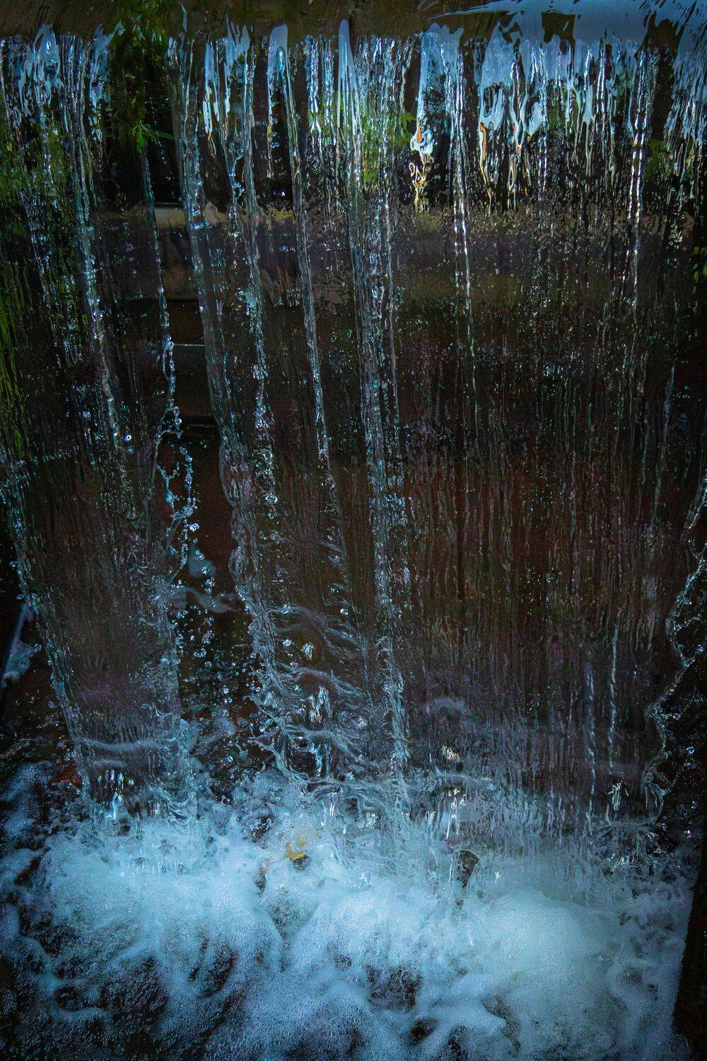 A beautiful small artificial waterfall with clear water splashing down into a dark old stone canal stream basin