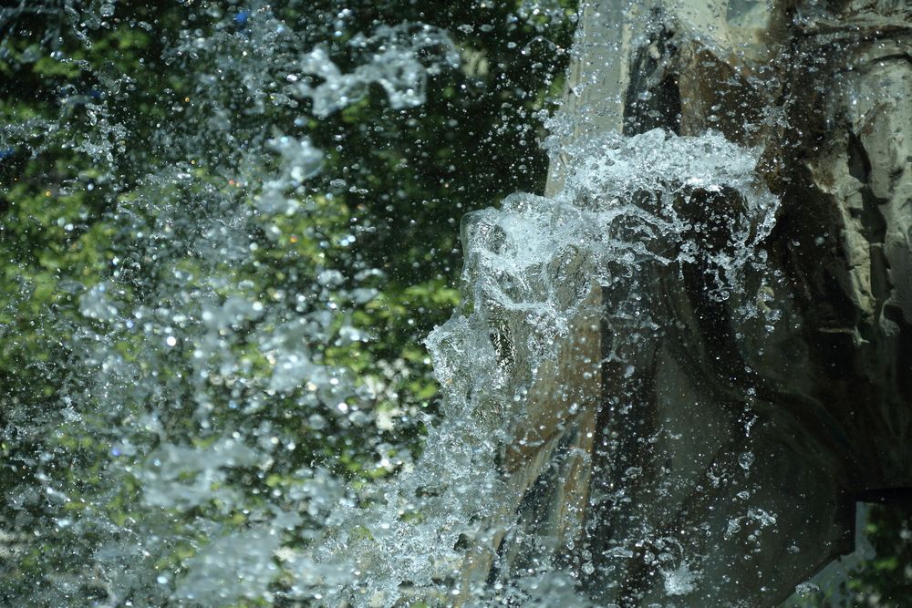 A dynamic high speed shutter photograph of clear water splashing and freezing in the air from a public fountain outdoors in summer