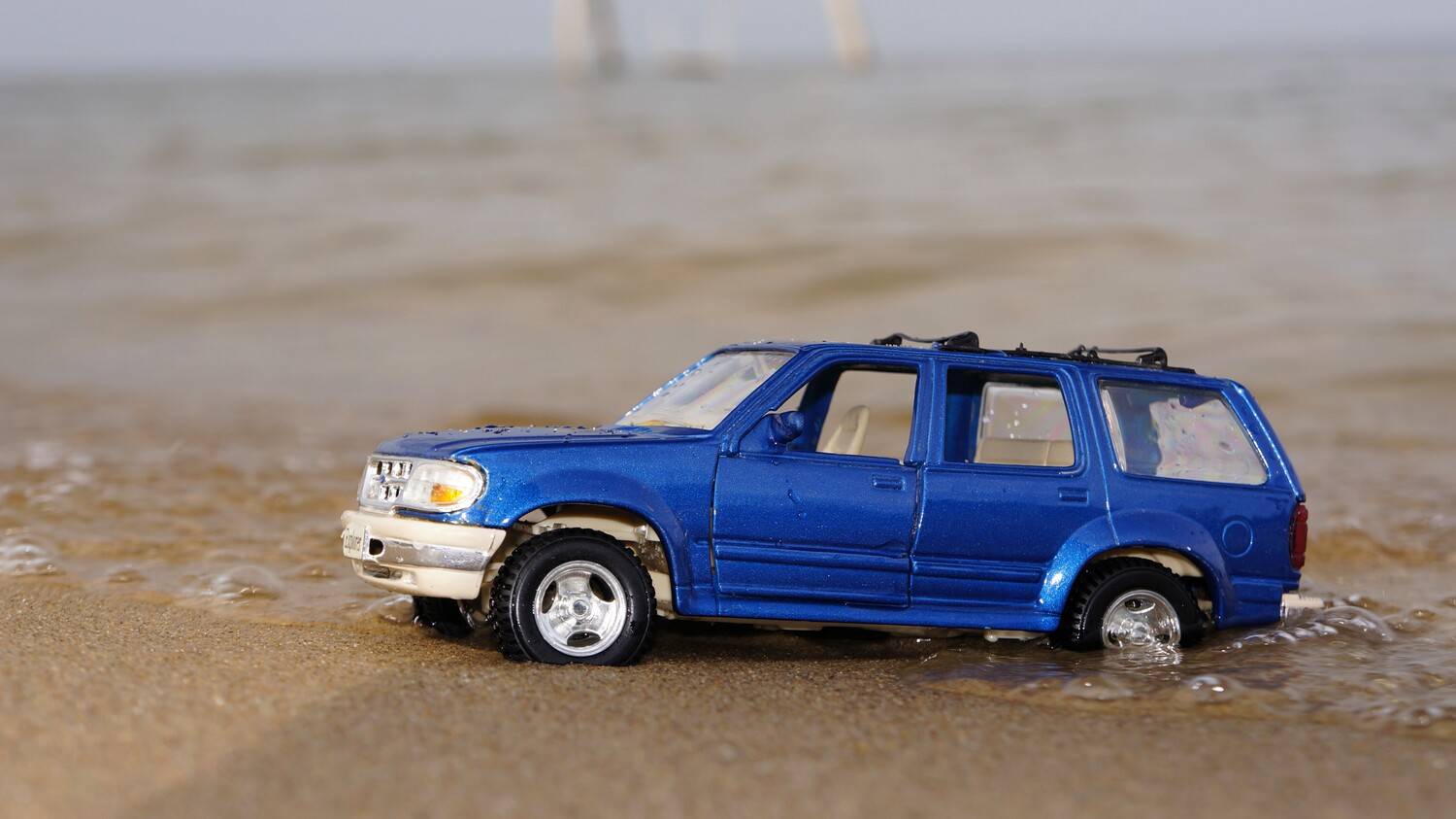 Коллекционная модель автомобиля Ford Explorer на песчаном пляже у кромки воды