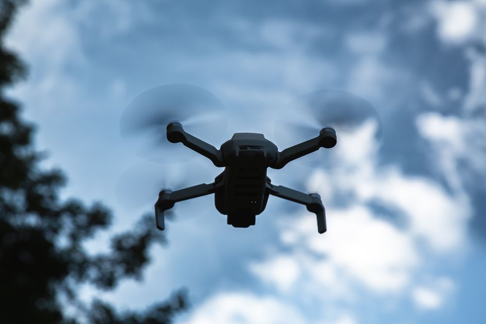 A spectacular low angle photograph focusing on a modern small white drone quadcopter flying high in the blue sky with spinning propellers