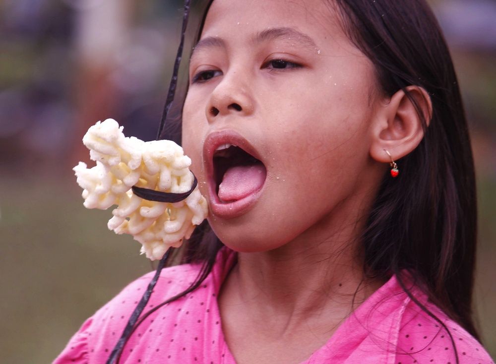 “The Sweetest Battle – A Girl’s Joyful Struggle with Hanging Cracker”