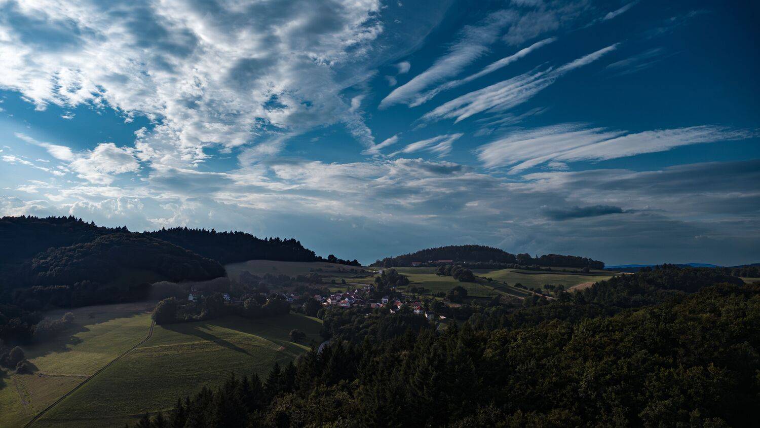 A magnificent high angle aerial drone photograph showing a peaceful village surrounded by dense picea abies spruce forests under a dramatic cloudy sky