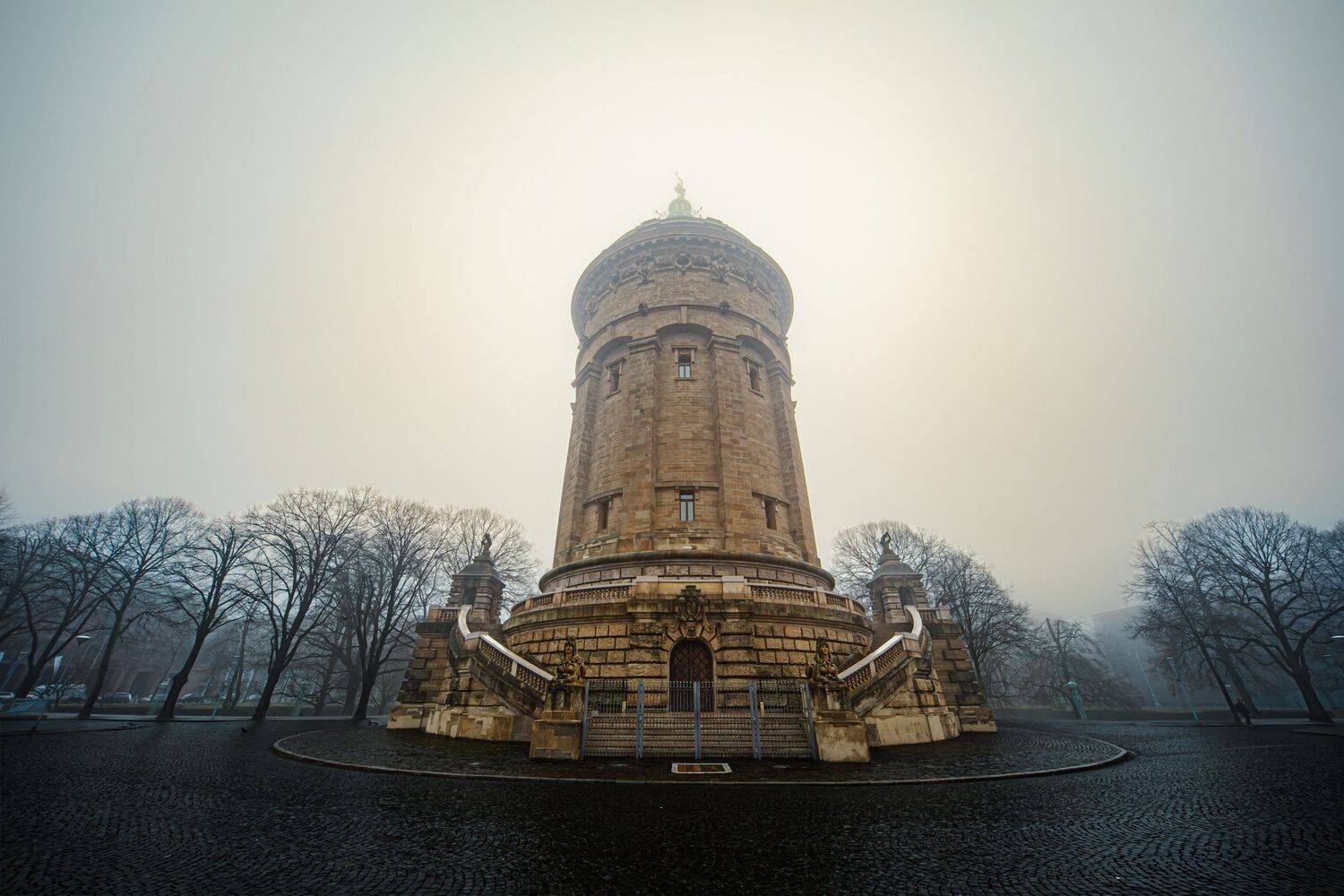 A magnificent symmetrical wide angle photograph showing the famous historical Mannheim water tower surrounded by acer platanoides maple trees inside a thick morning fog