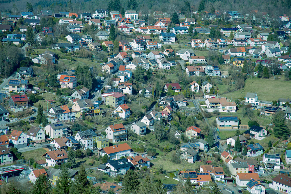 A beautiful detailed high angle landscape photograph showing many residential village houses and green pine trees upon a sunny hill during a bright spring day