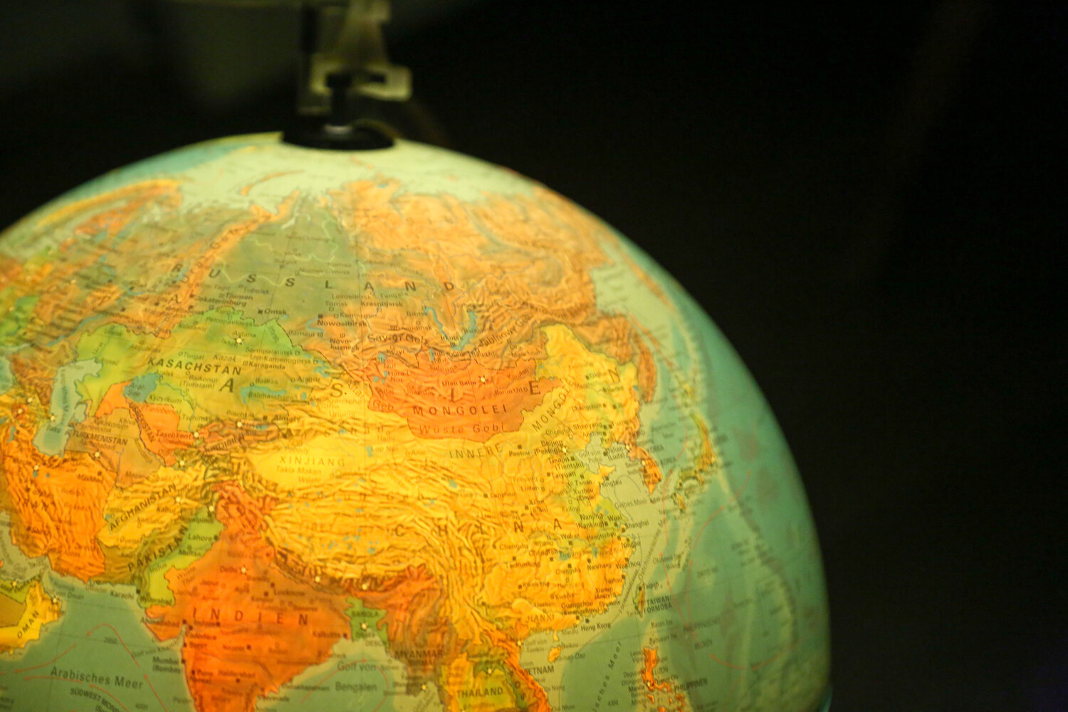 A detailed close up photograph showing a colorful vintage terrestrial globe map focus on eurasia continent against a dark background during a sunny day