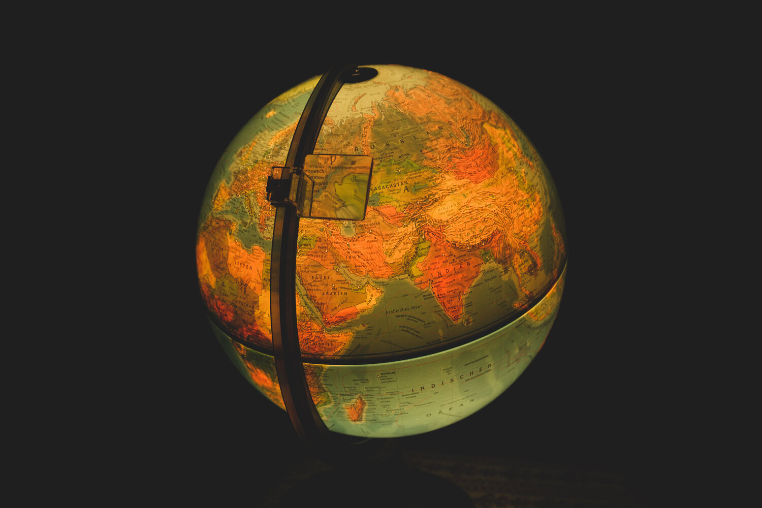 A beautiful detailed close up conceptual photograph showing a glowing vintage illuminated terrestrial globe map with eurasia continent details against a dark black background during a sunny day