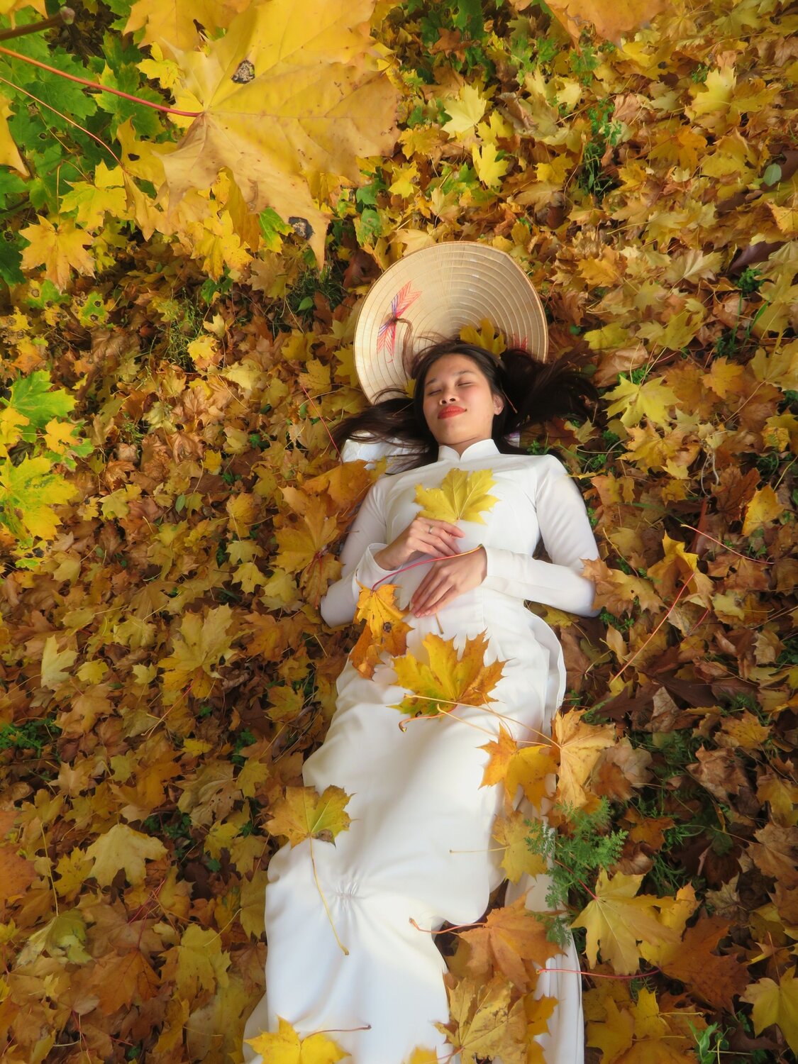 Woman in white Ao Dai lying on yellow autumn yellow leaves