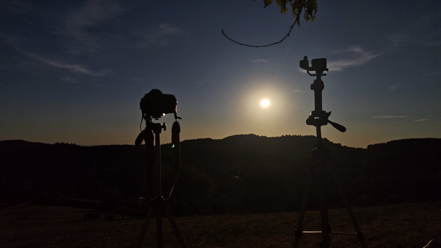 A detailed wide photograph showing camera and action camera on tripods filming dark golden sunset silhouette over mountain hills