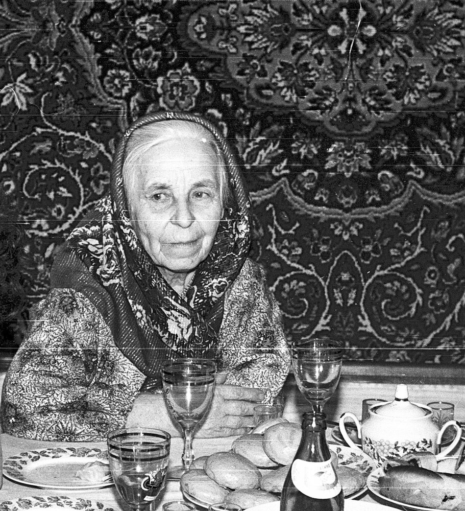 Пожилая женщина, сидящая за праздничным столом в доме