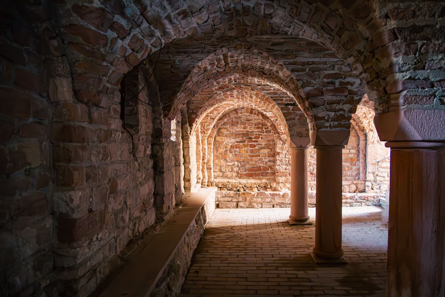 A detailed wide interior photo showing historic medieval stone crypt with arched brick vaults sturdy round columns and brick floor