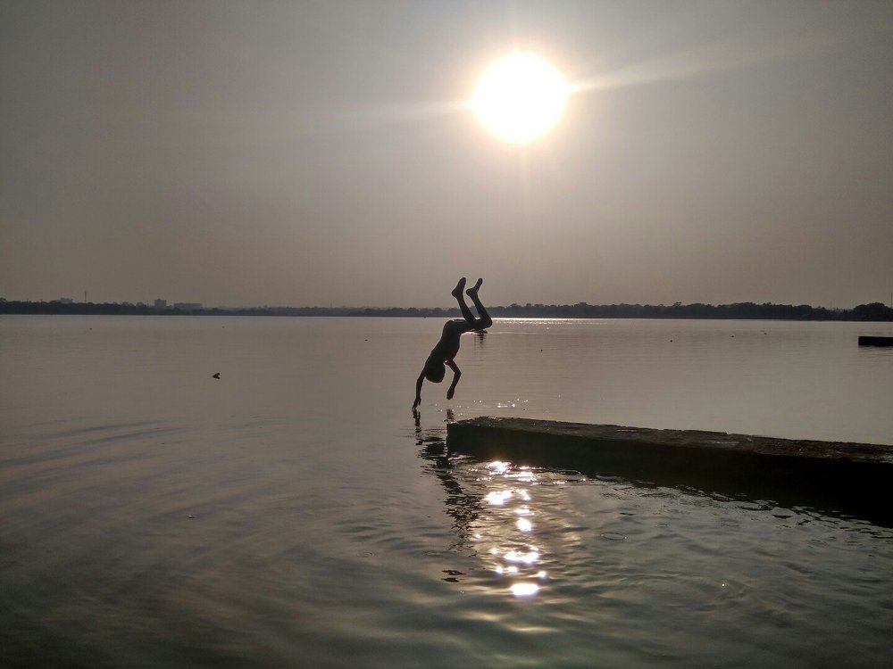 small boy div at water at time of sun set